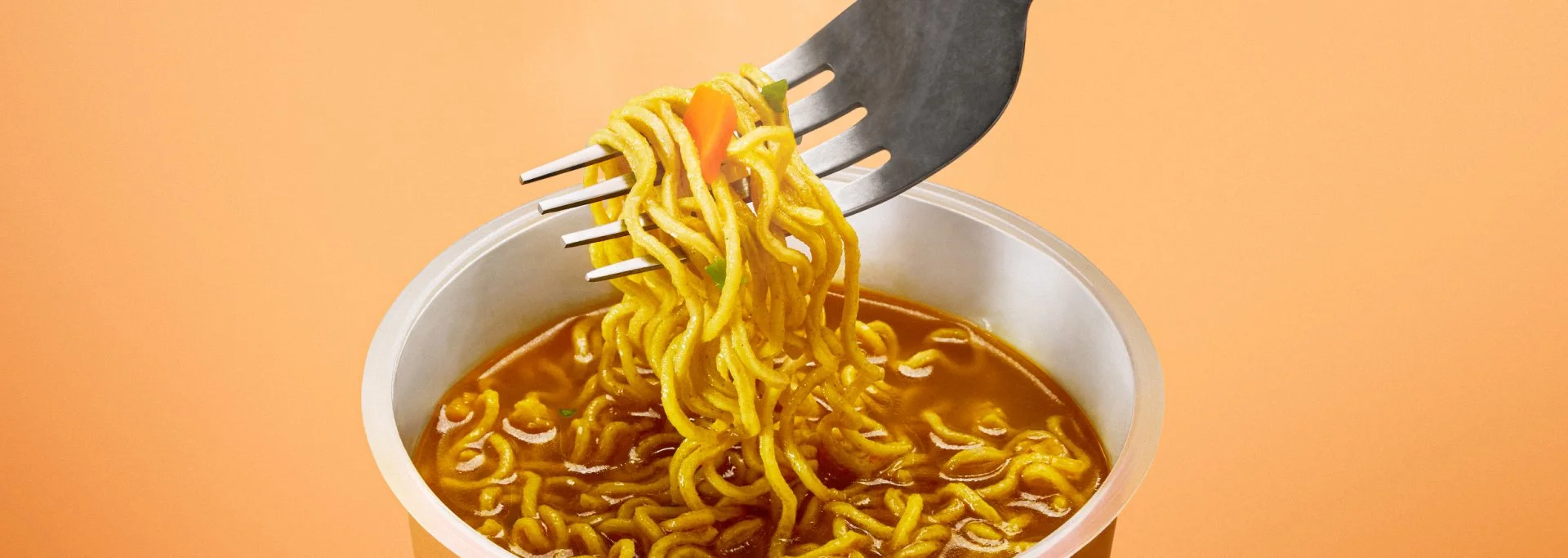 A fork lifting yellow noodles with vegetables from a cup of hot, spicy ramen.