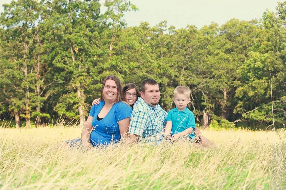 Family of four sitting in a grassy field with trees in the background