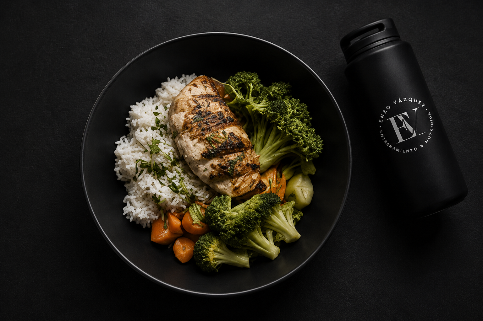 Plato de arroz con pollo a la parrilla, brócoli, zanahorias y cilantro en un plato negro, junto a una botella negra de agua con logotipo y texto en blanco.