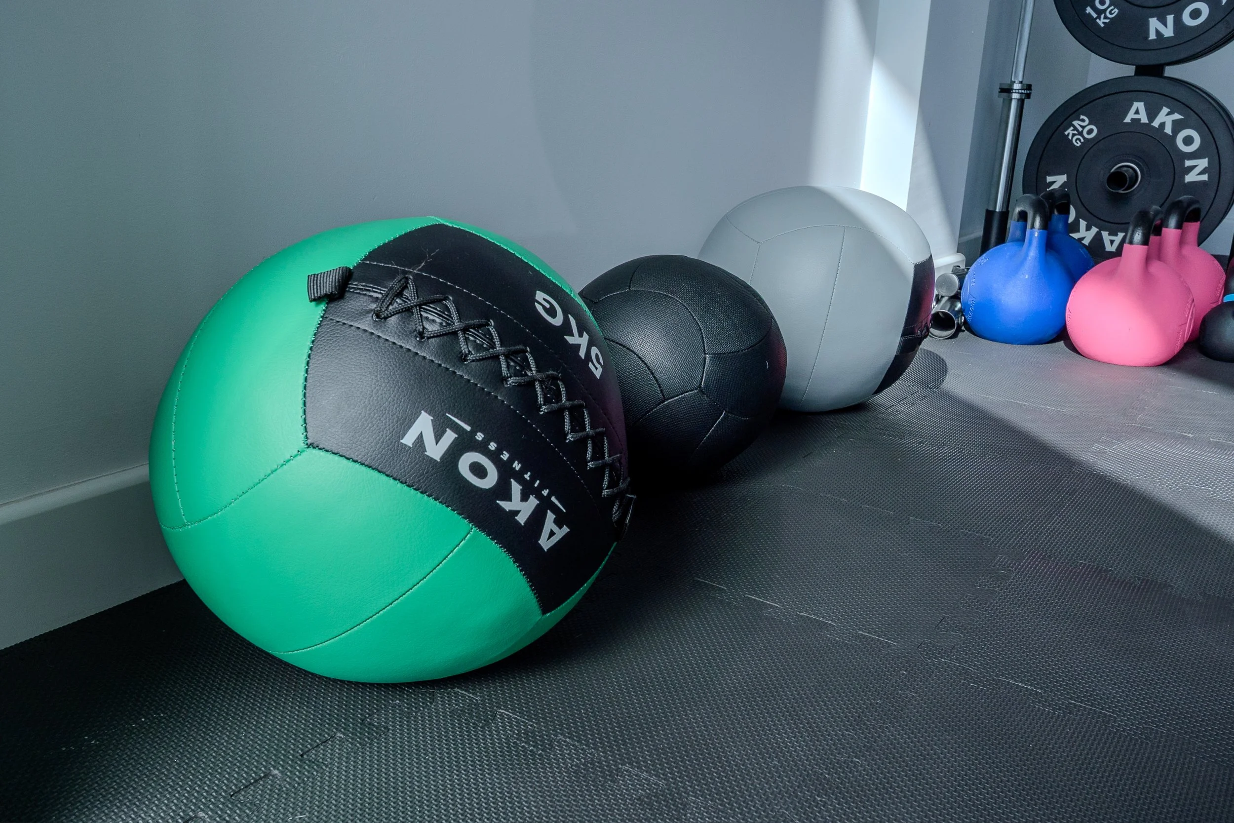 Equipo de ejercicio en un gimnasio, incluyendo una pelota de gimnasia azul y varias pesas y kettlebells de colores
