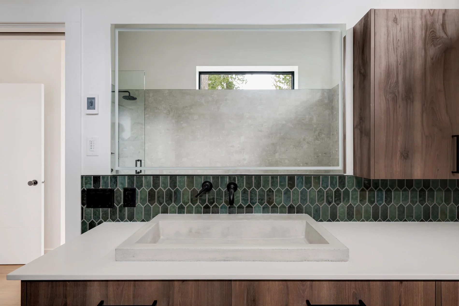 Modern bathroom with a large mirror, tiled shower area, black fixtures, and a wooden vanity with a white countertop.