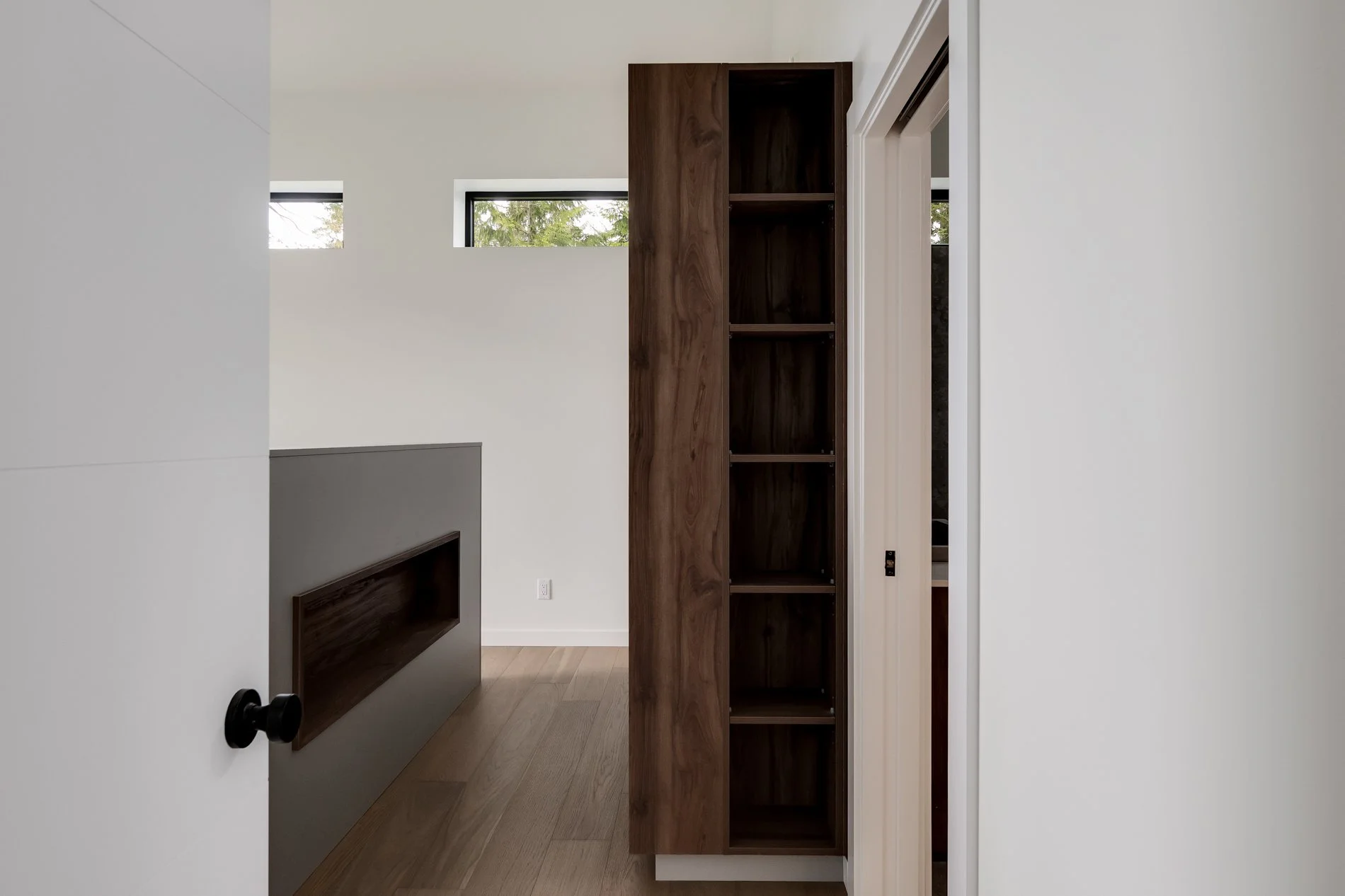 Interior view of a modern room with a tall wooden bookshelf with empty shelves, a partial view of a fireplace, and a door partially open.