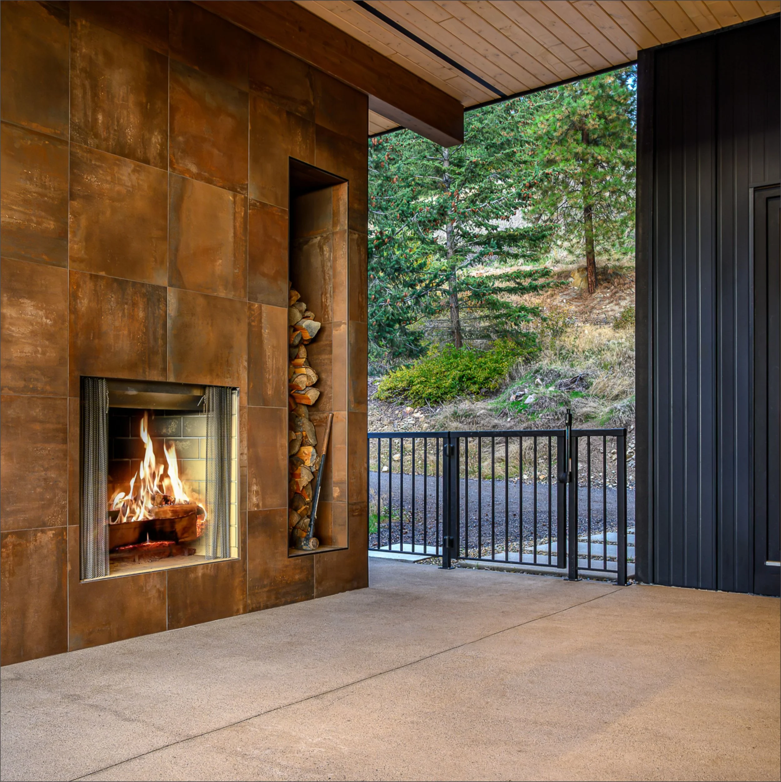 Indoor space with a modern fireplace, tiled wall, and a large window showing trees outside.