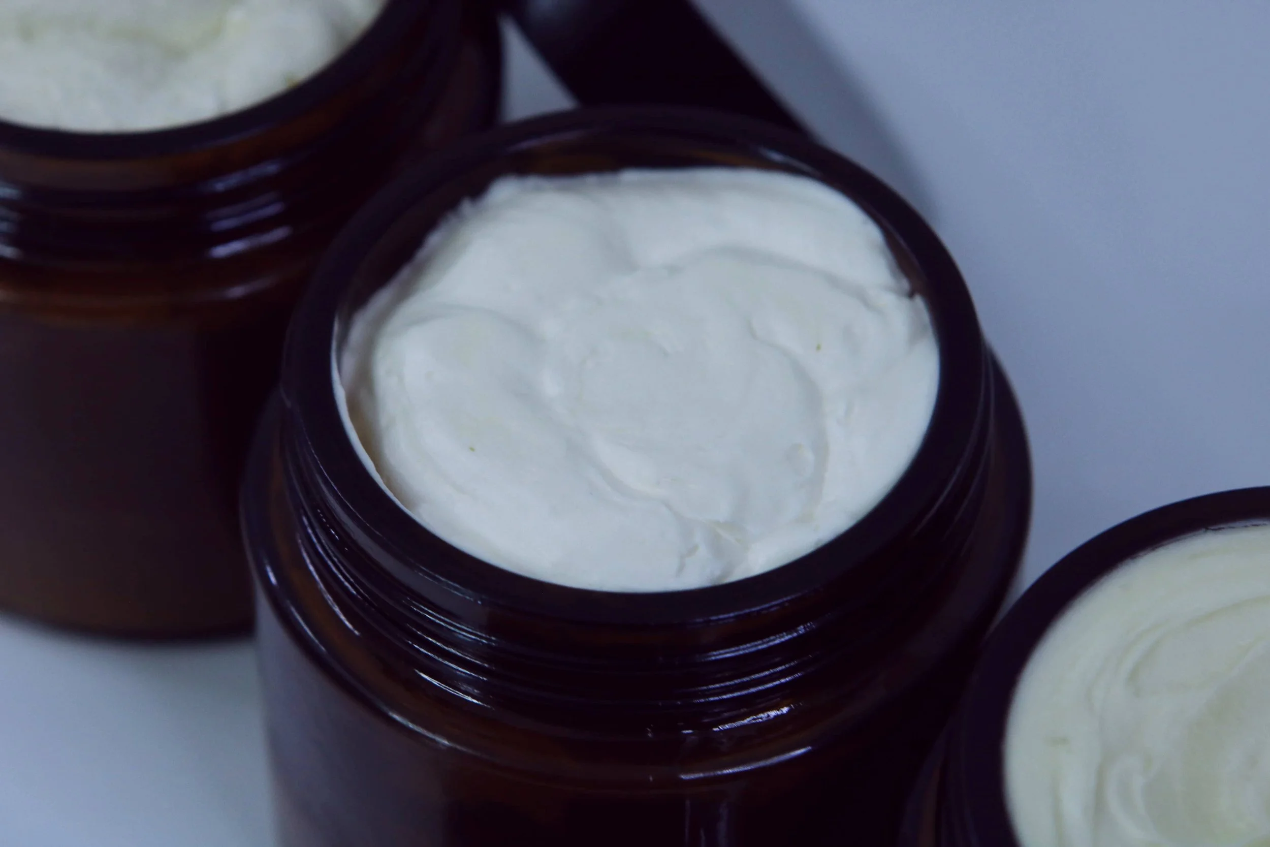 Close-up of open brown jars filled with body butter, viewed from above.