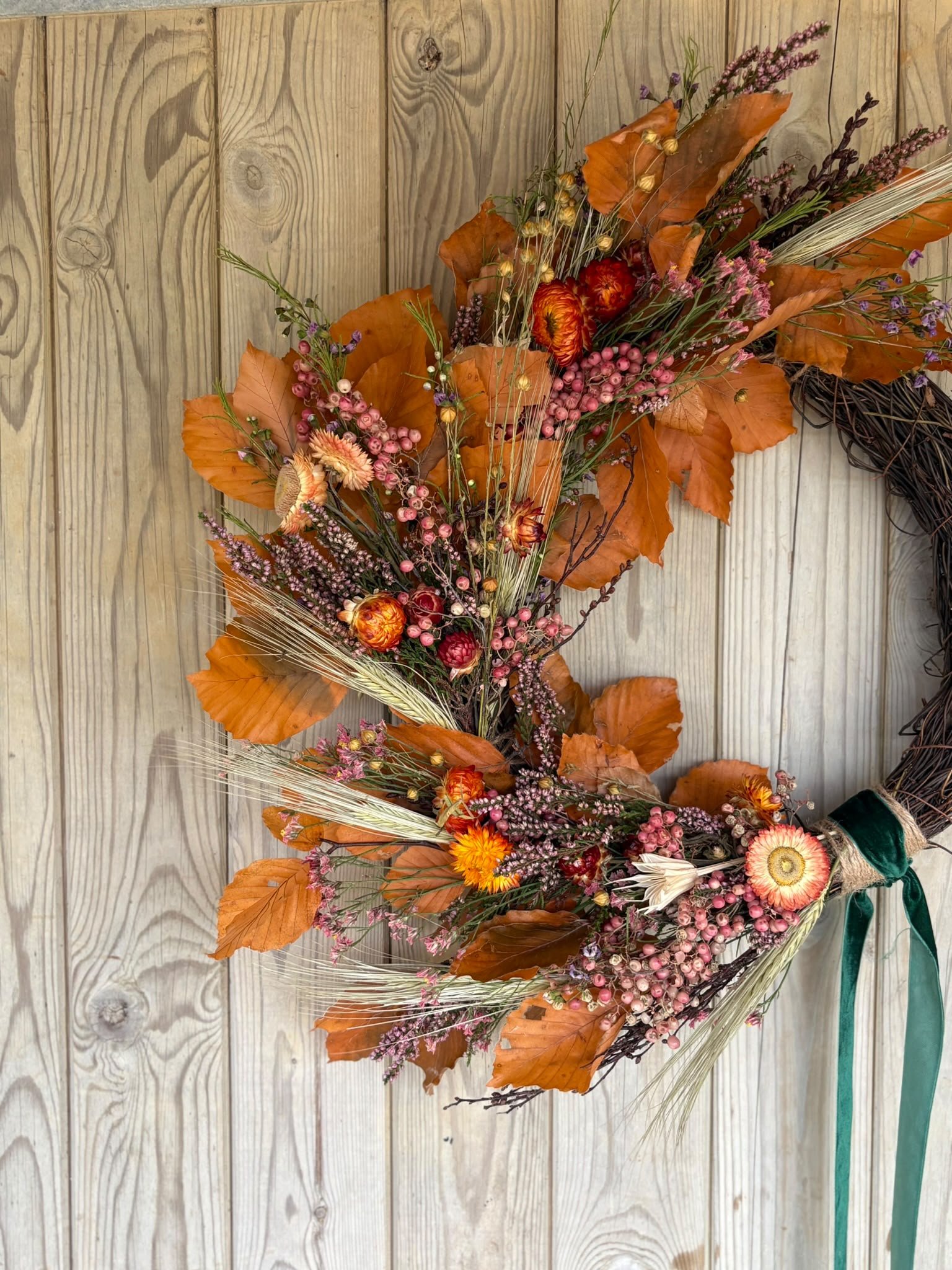 Autumn-themed floral arrangement with dried leaves, pink berries, and various flowers, displayed on a wooden surface.