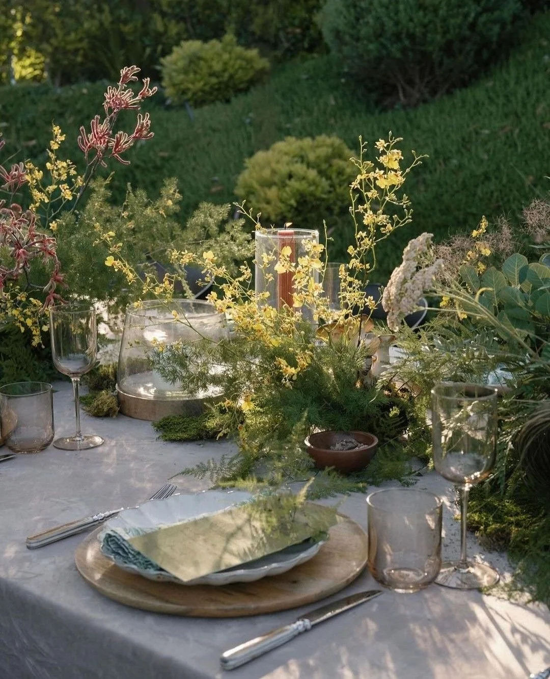 Elegant outdoor dining table with floral centerpiece, glassware, and tableware, set in a garden with lush greenery.