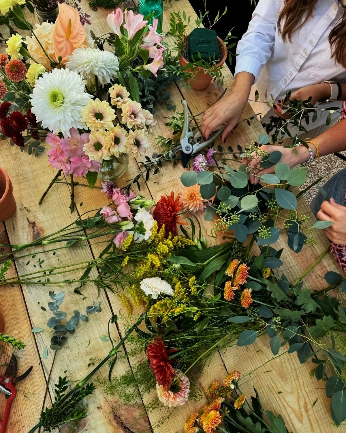People creating floral arrangements with various colorful flowers and green foliage on a wooden table.