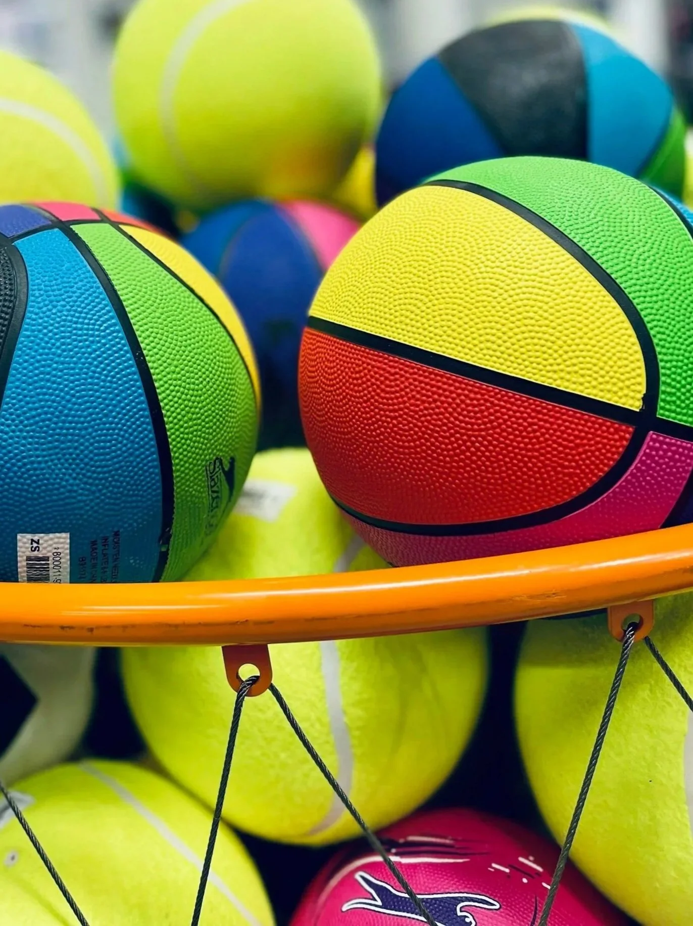 Colorful rubber balls stored in a basket, including yellow, green, pink, blue, and black, with some patterned in a three-color design.