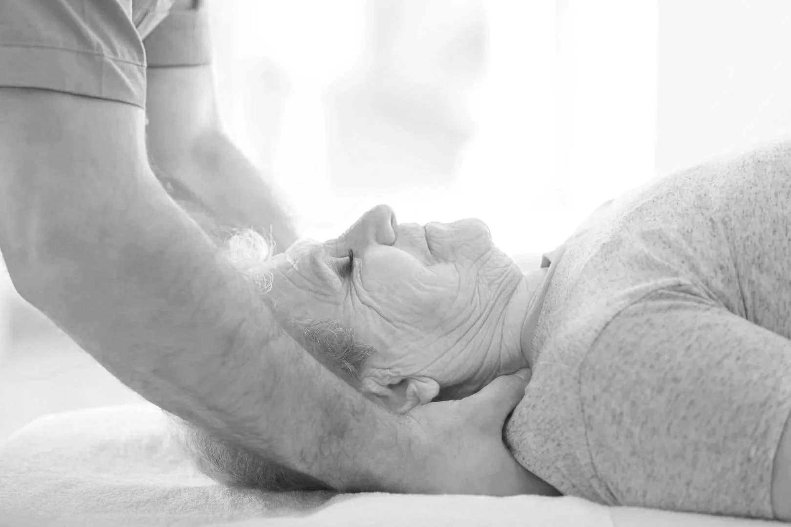 Une personne âgée allongée, tenant la tête d'une autre personne allongée, dans une scène tendre et intime.