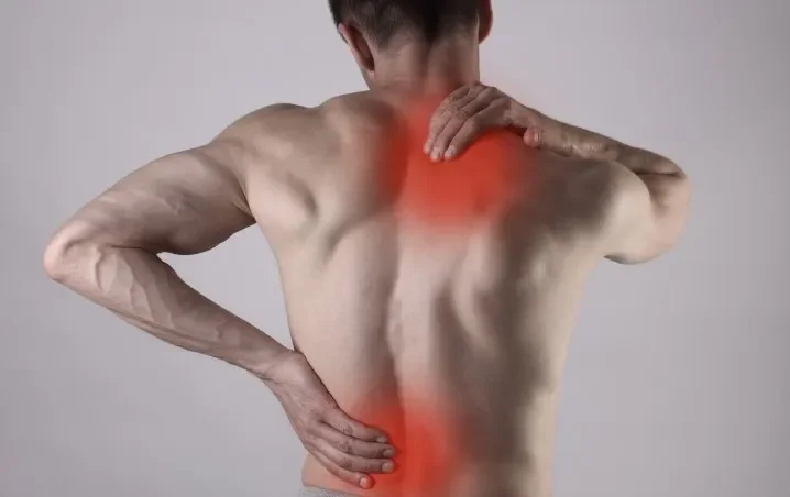 Un homme nu vu de dos, se tenant le dos avec une main et la nuque avec l'autre, la zone du dos est en surbrillance rouge, indiquant de la douleur ou une blessure.