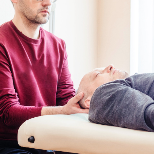 Un homme allongé sur une table de consultation, une autre personne le touche au cou.