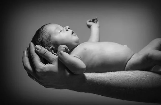 Un nouveau-né pacifiquement endormi dans une main humaine, en noir et blanc.