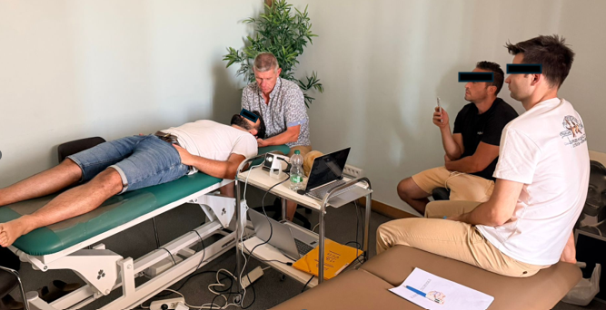 Un patient allongé sur une table d'examen dans un cabinet médical, plusieurs jeunes personnes assises à côté, utilisant des appareils électroniques.