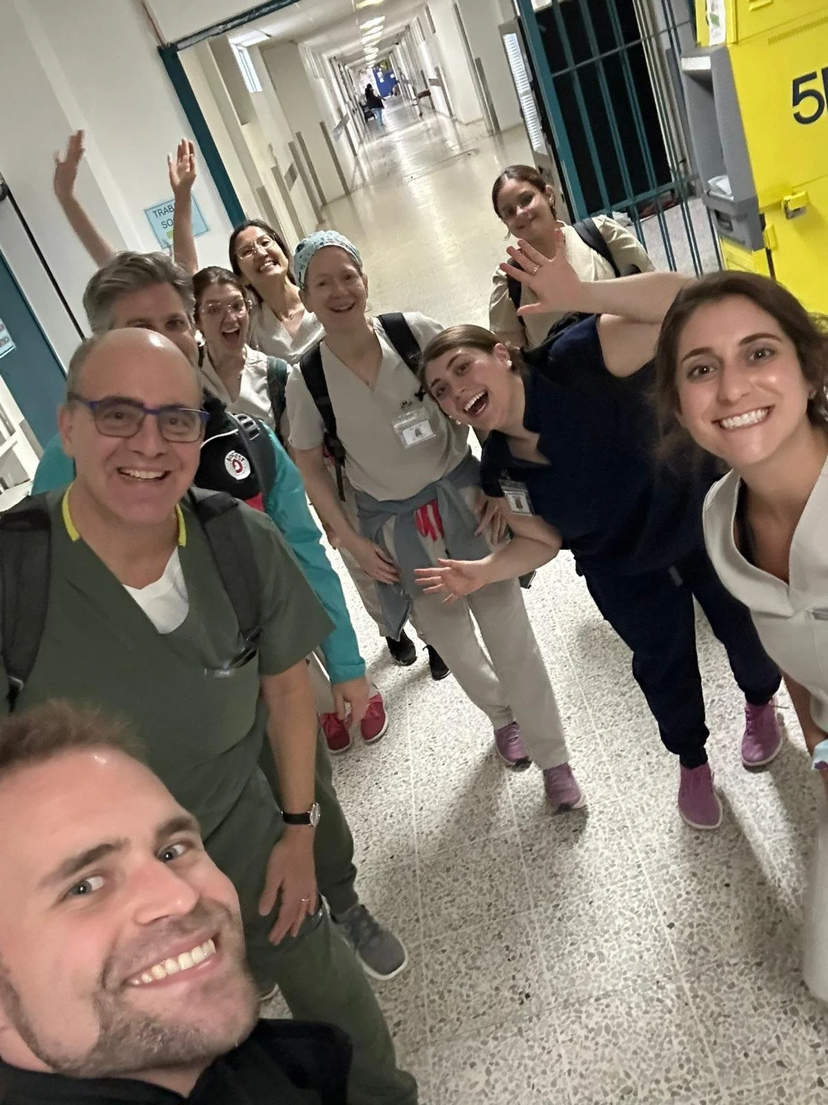 A group of smiling medical professionals taking a selfie in a hospital corridor, some making playful gestures.