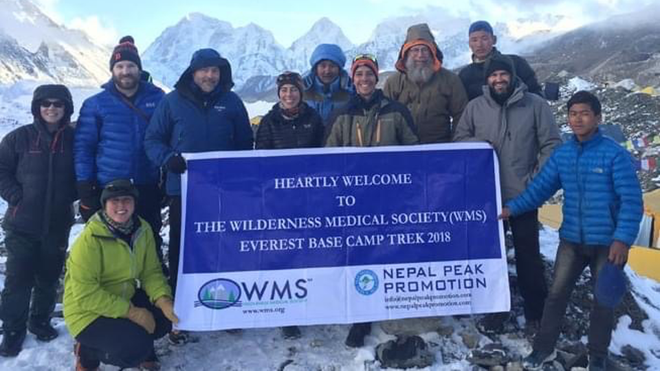 Group of people holding a banner at Everest Base Camp surrounded by snow and mountains.