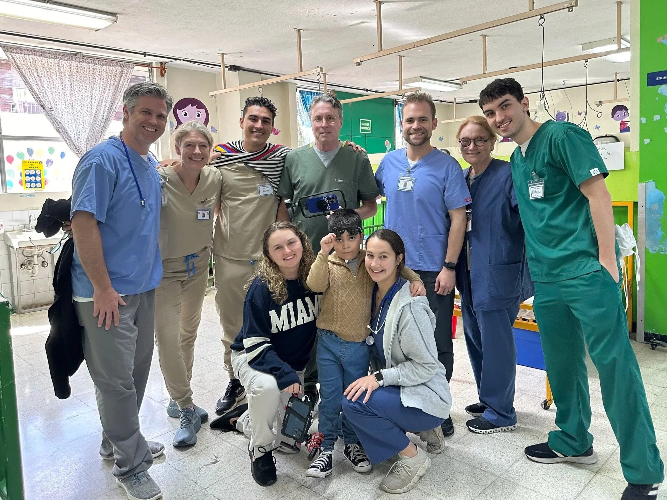 A group of healthcare professionals and children posing for a group photo in a pediatric hospital room.