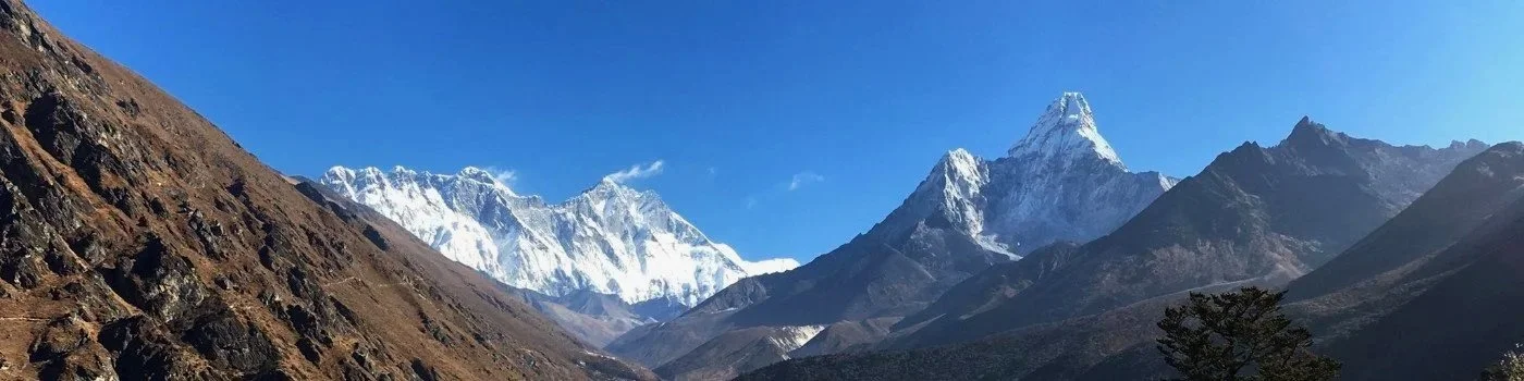 Snow-capped mountains under a clear blue sky with some rocky slopes in the foreground.