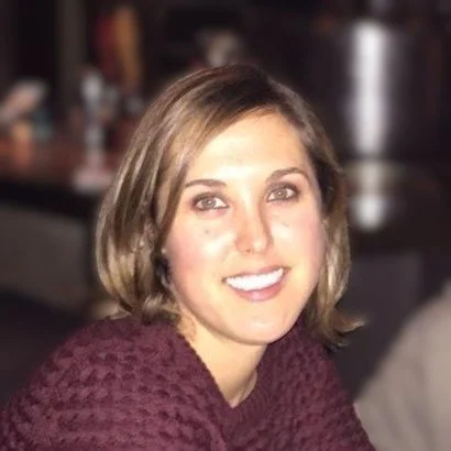 A portrait photo of Megan Rand smiling for the camera, with shoulder-length hair and wearing a maroon sweater.