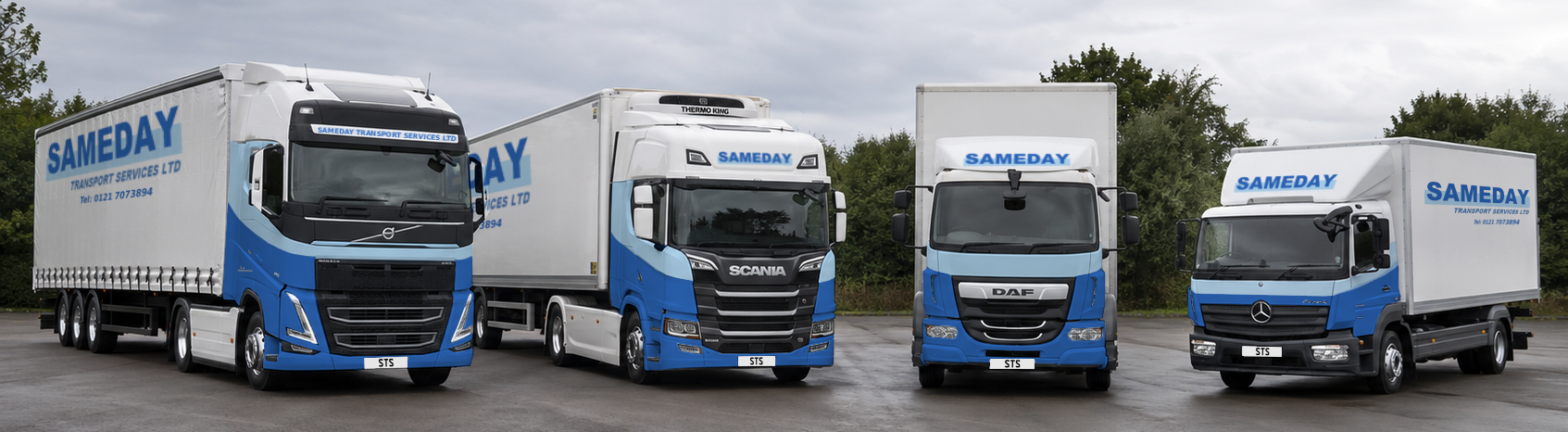 Four freight trucks parked on a paved lot with trees and cloudy sky in the background. Each truck has the company name ’SAMEDAY’ prominently displayed on the front and sides, with different makes and models.