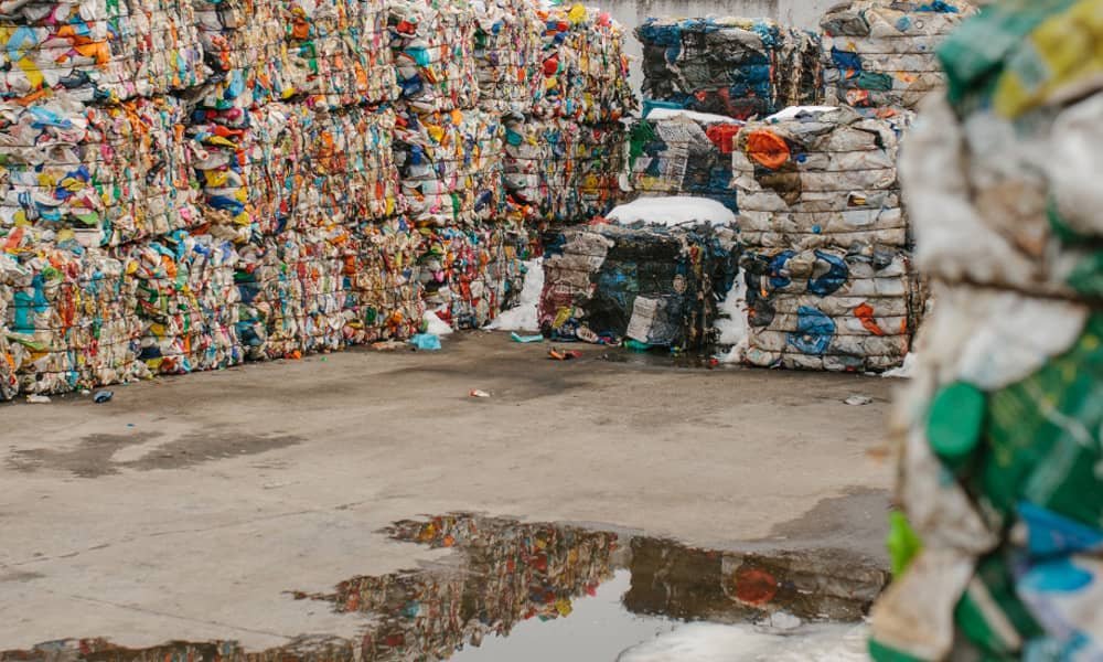 Large stacks of compressed recyclable plastic bottles and packaging materials in an industrial recycling facility.