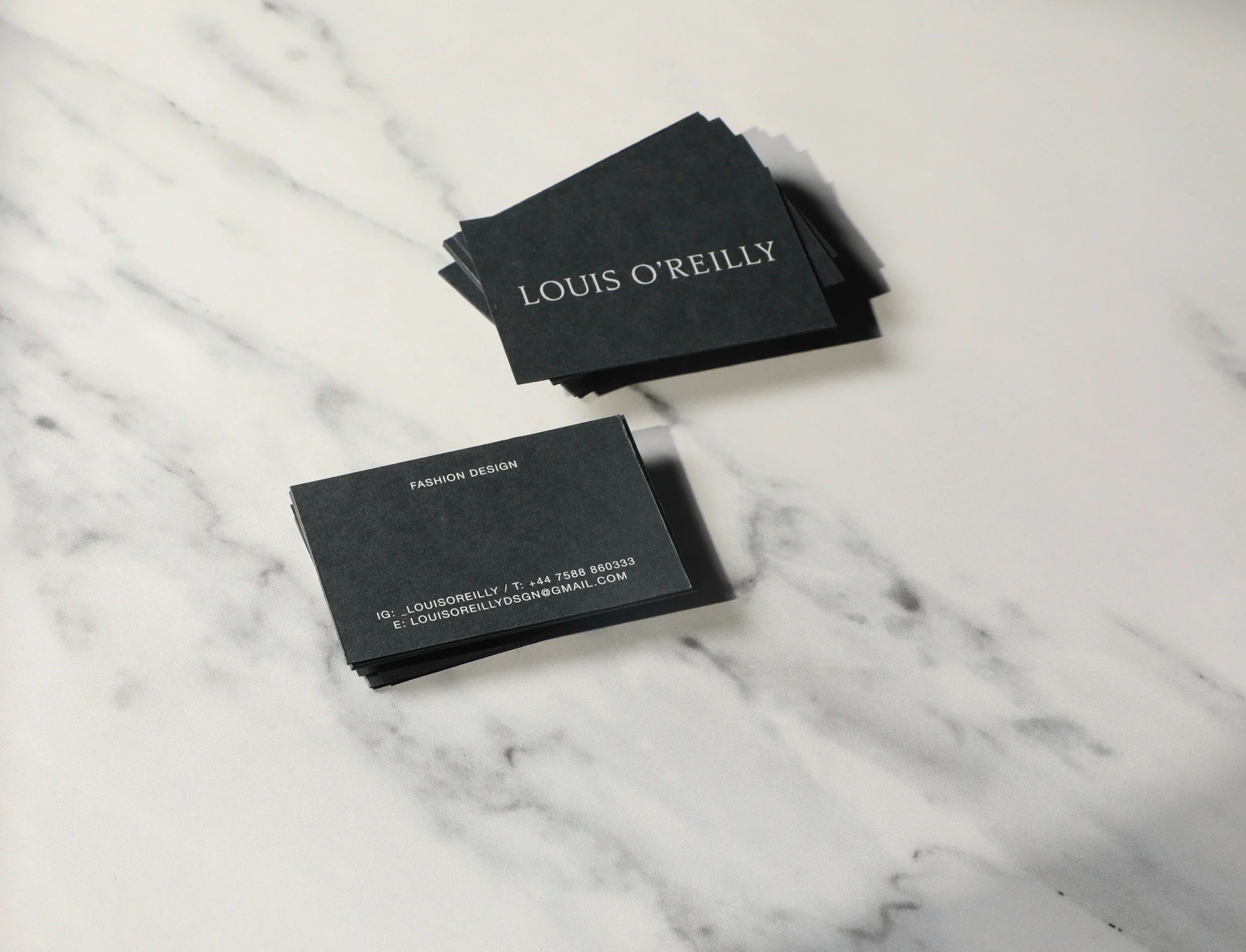Stack of black business cards on a white marble surface, with the top card reading "Louis O'Reilly".