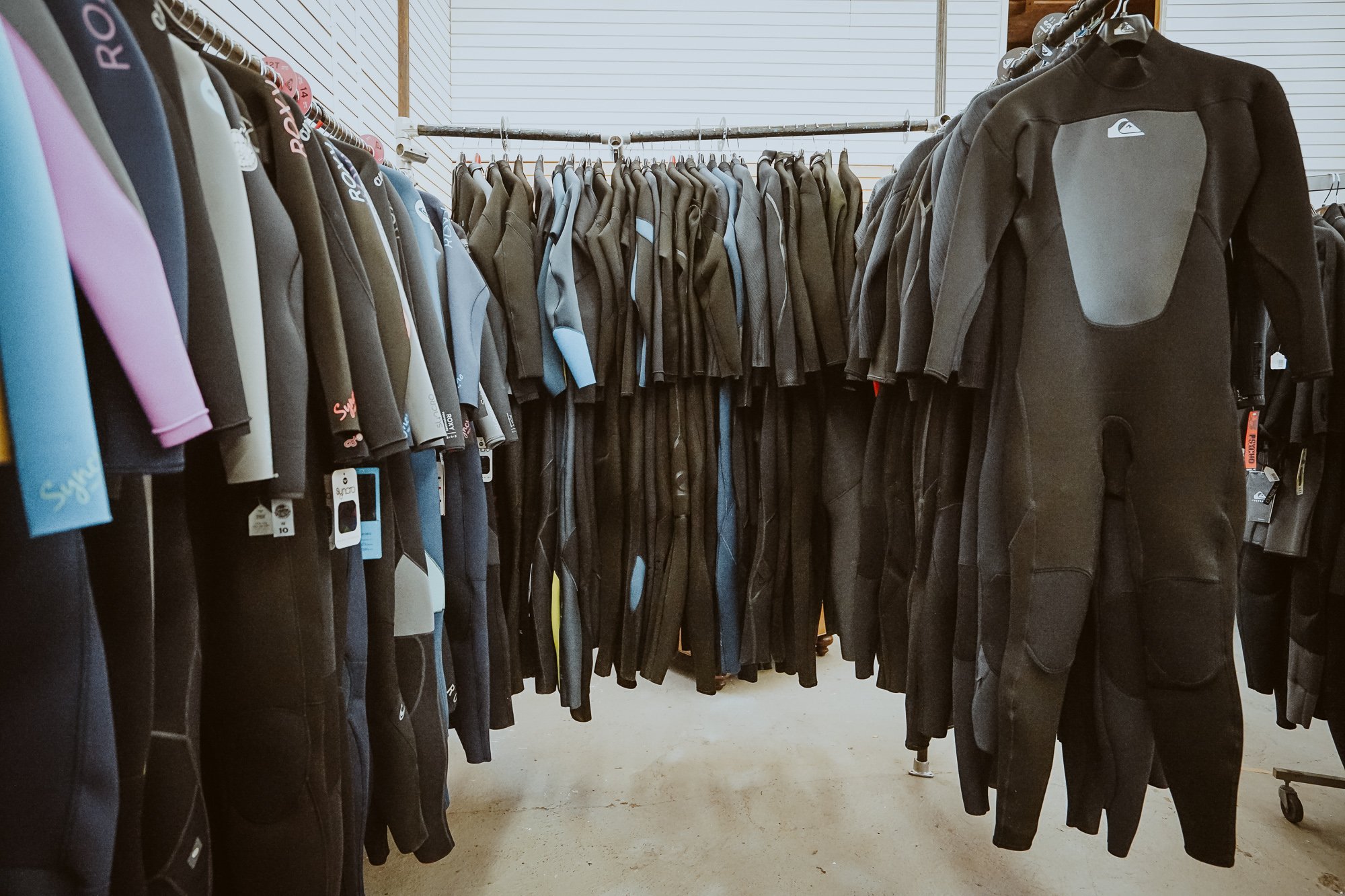 Clothing rack filled with wetsuits and neoprene jackets in a retail store.