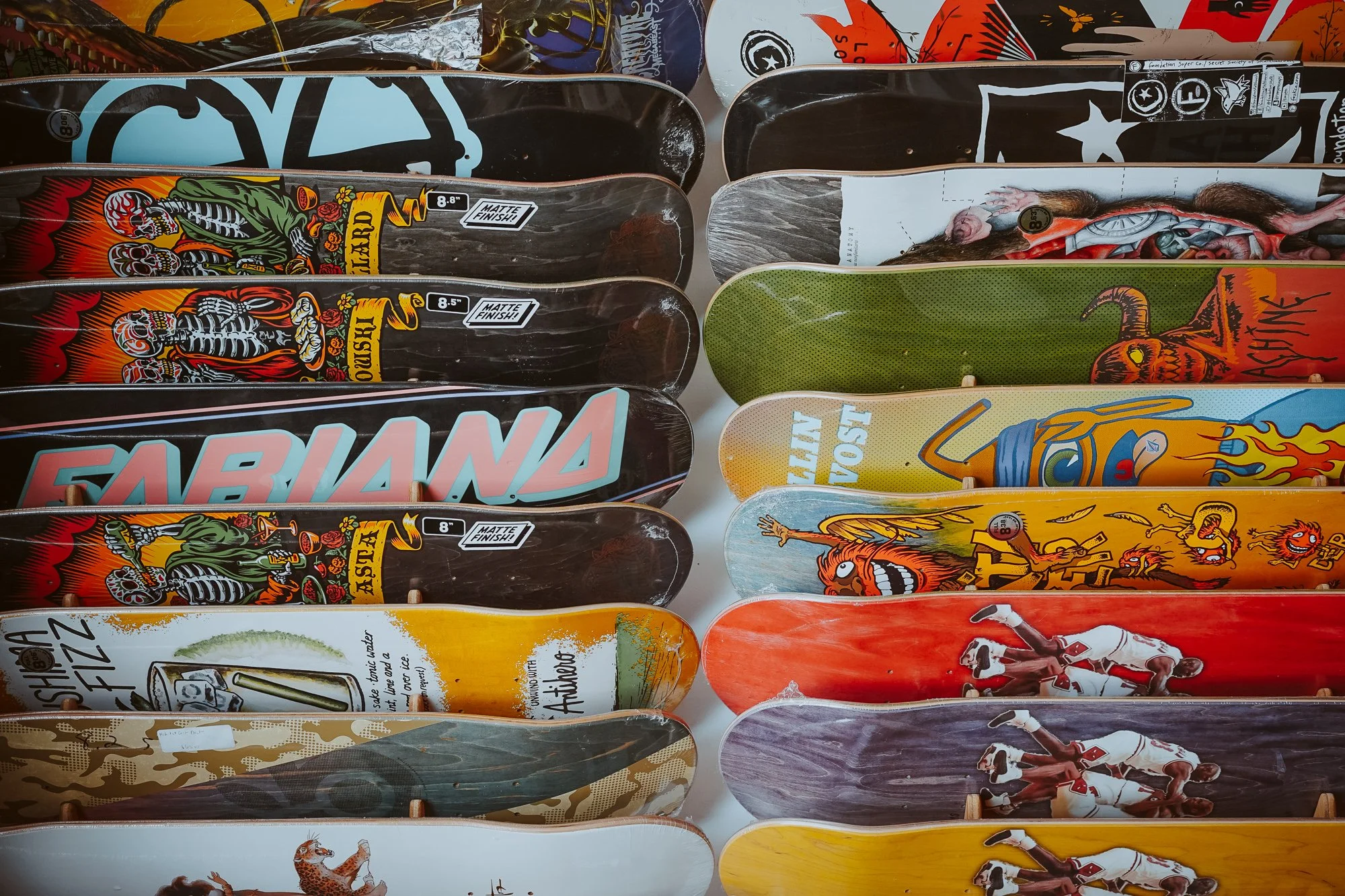 A collection of skateboard decks with various colorful and graphic designs, including skeletons, animals, and abstract art.