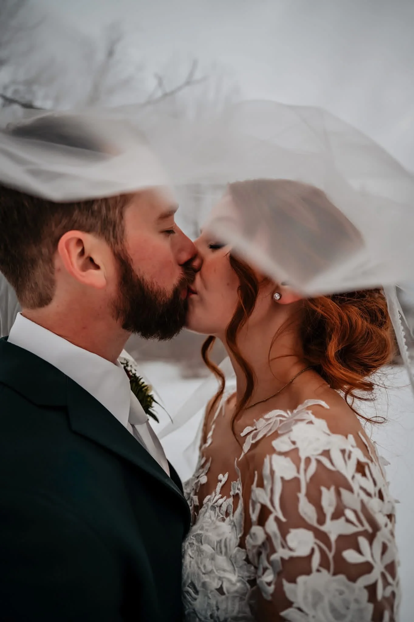 A couple sharing a kiss at their wedding, with the groom in a tuxedo and the bride in a white lace dress.
