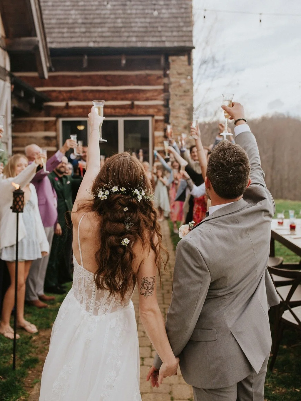 Bride and groom holding glasses in a toast at an outdoor wedding celebration, surrounded by guests.