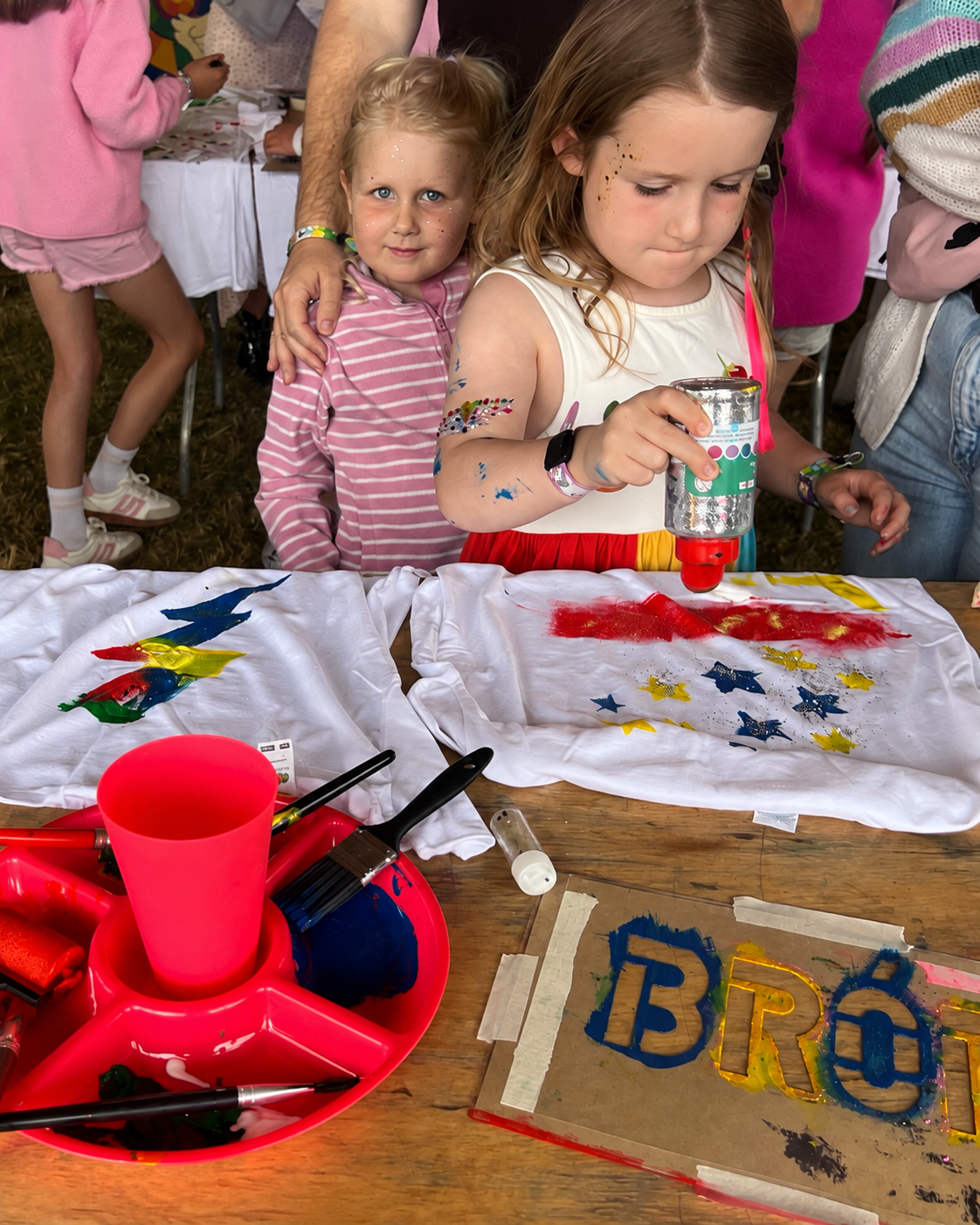 Children creating arts and crafts with fabric, paint, and glitter at a craft table, celebrating a patriotic theme with star and flag designs.
