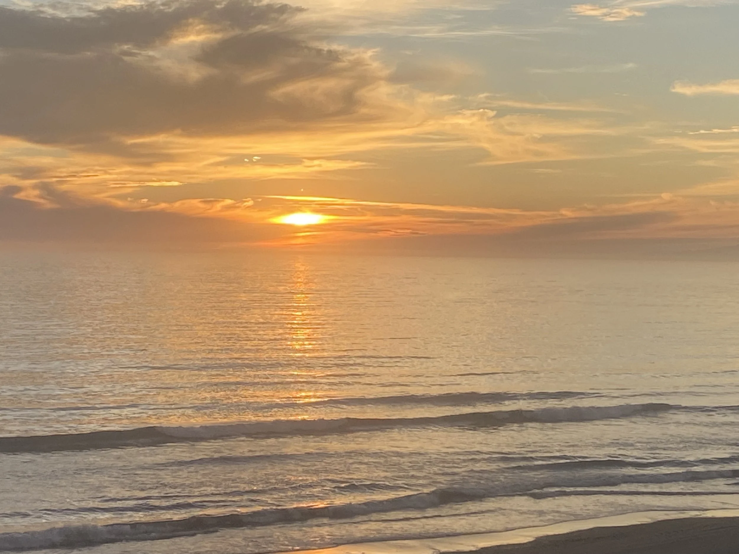 Sun setting over calm ocean waters with changing colors in the sky and clouds.