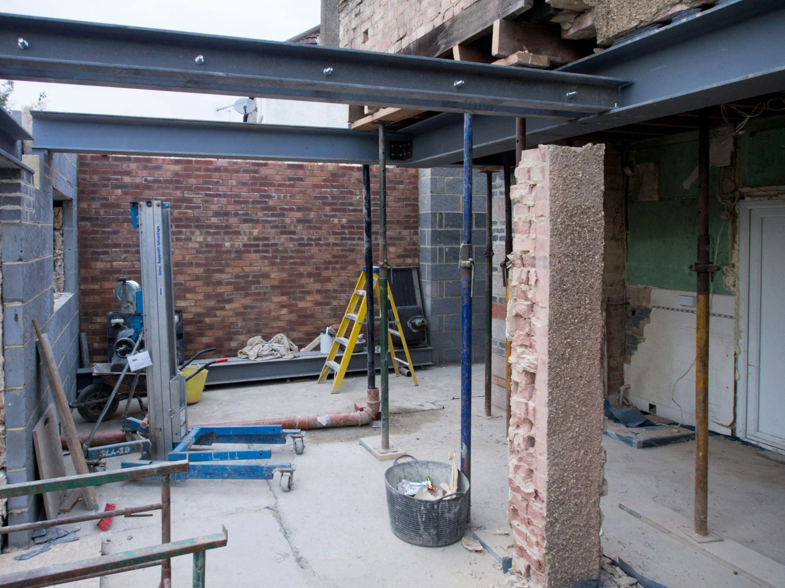 Construction site with exposed brick and concrete walls, metal beams, scaffolding, ladders, and construction tools.