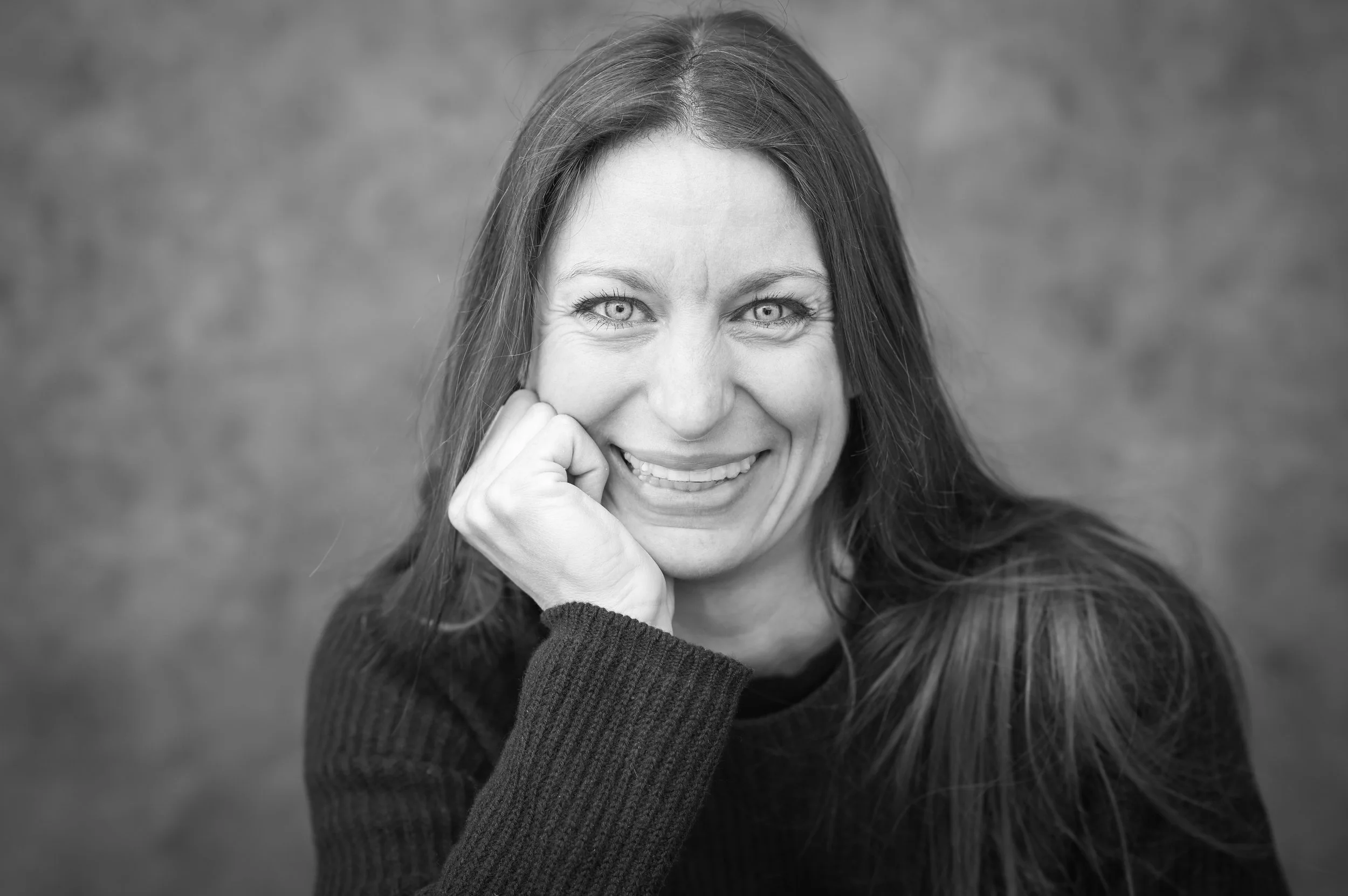 Black and white photo of a woman with long hair smiling, resting her face on her hand.