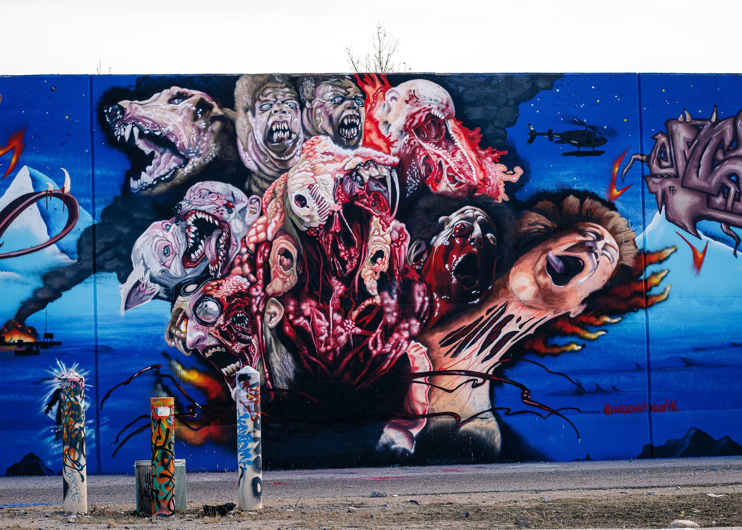 Colorful graffiti mural depicting monstrous faces and creatures on a blue background, with two spray paint cans with graffiti art on them in the foreground.