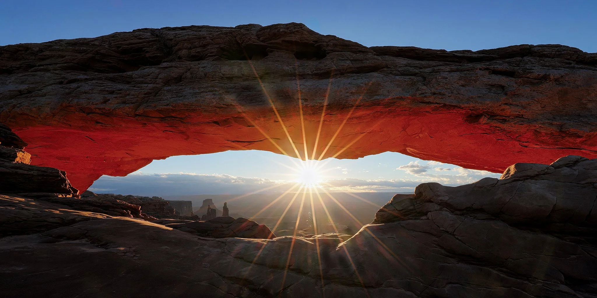 Sunset viewed through a natural rock arch with a red hue at sunset in a desert landscape
