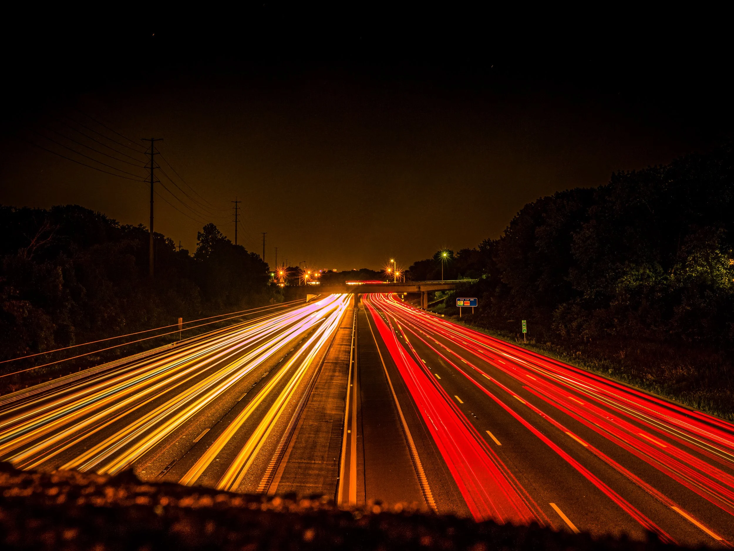 Long exposure night photograph of red and gold light trails on Interstate 64 in St. Louis, converging toward an overpass under a black sky