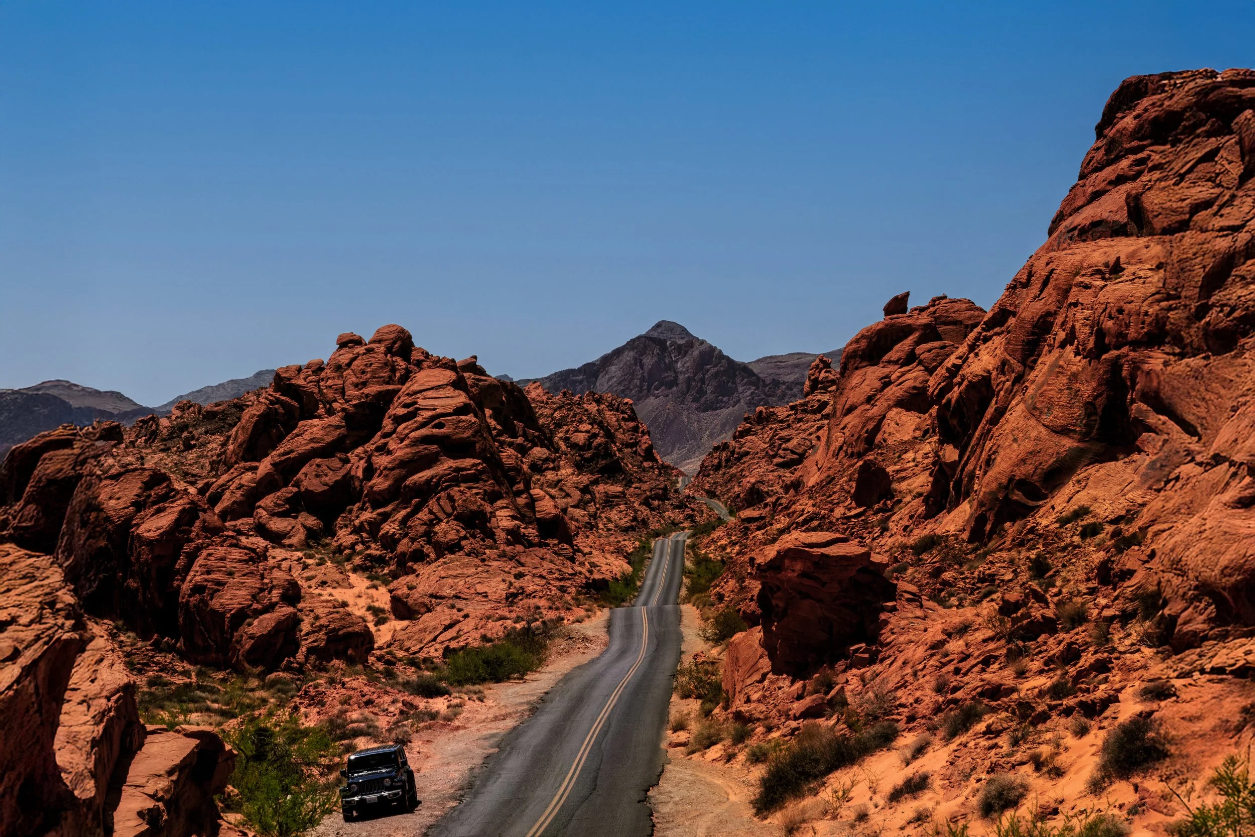 A winding road through red rocky desert landscape with mountains in the background under a clear blue sky.