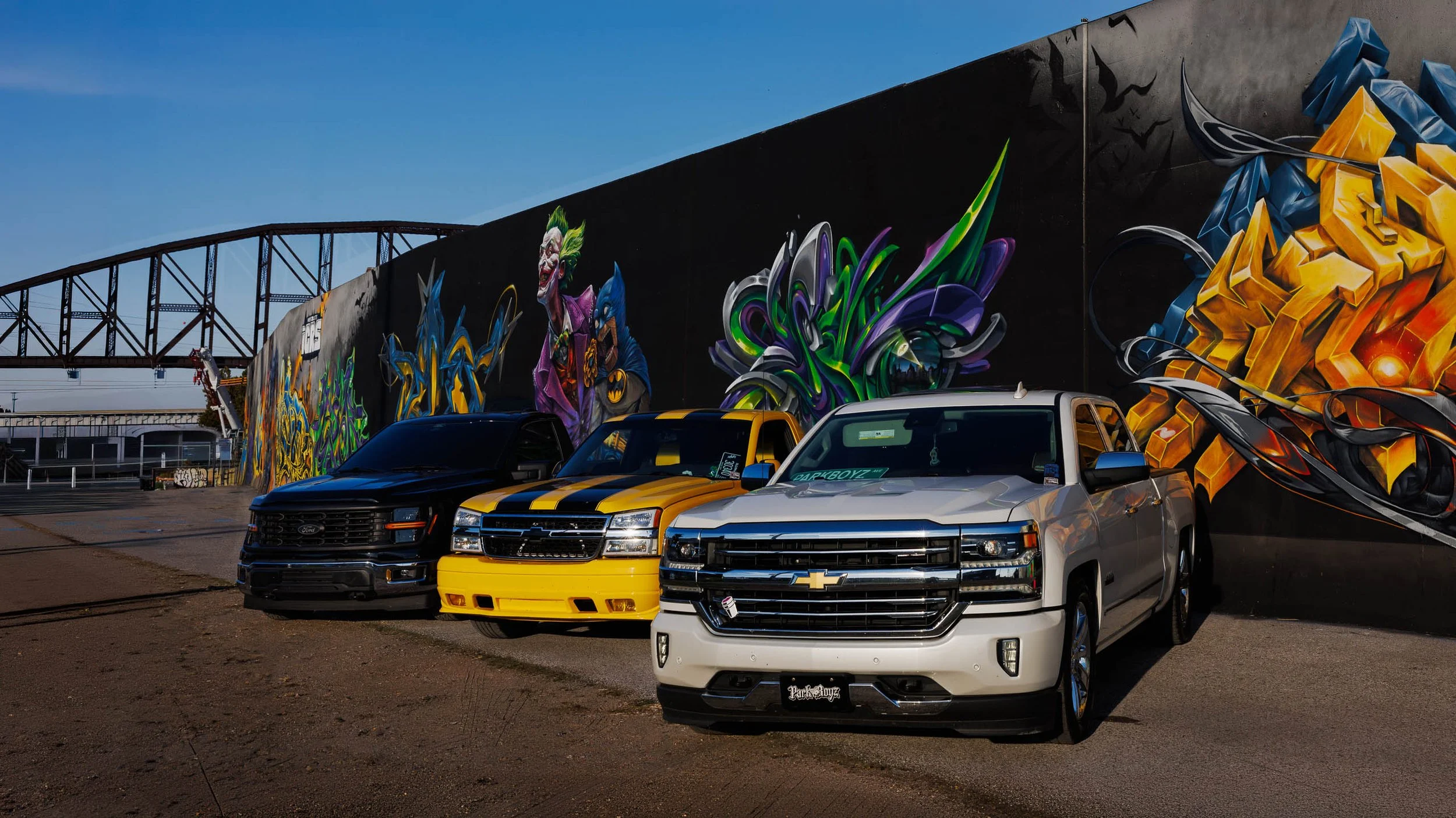 Black Ford, yellow striped Chevy and pearl Silverado parked before a black St. Louis mural with gold lettering