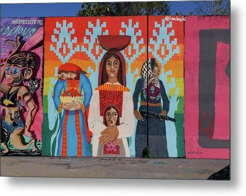 Mural of three standing figures in embroidered dress before horizontal rainbow bands and stepped pale-blue motifs on a wall in St. Louis, the center figure balancing a bowl on her head