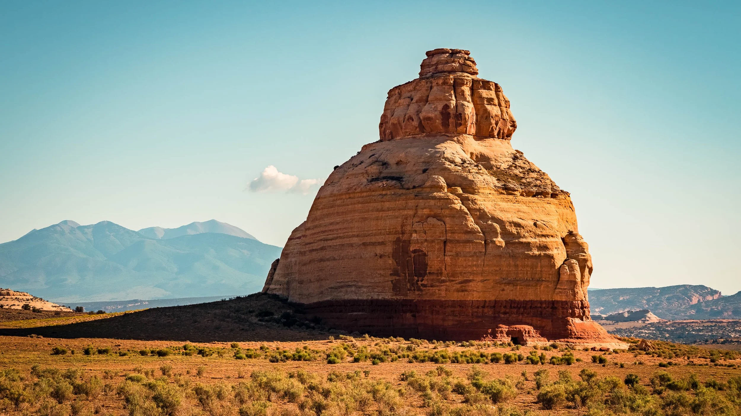 Orange sandstone monolith Church Rock under a pale blue sky with the La Sal Mountains behind, near Moab, Utah