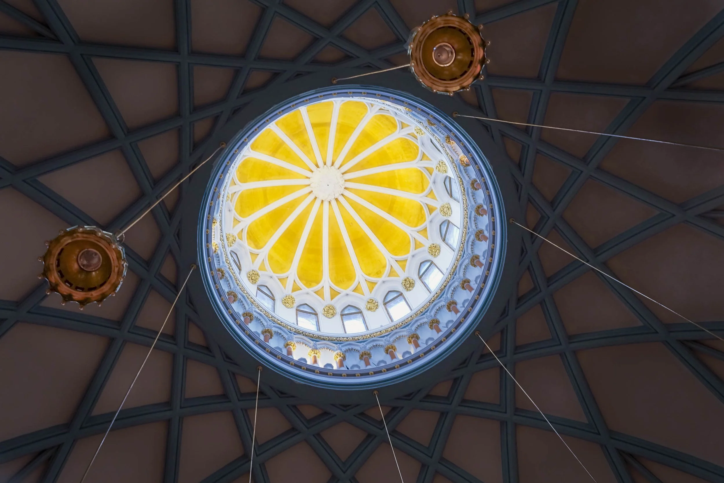 Looking up into a ribbed ceiling on Parliament Hill in Ottawa: a gold dome with white ribs ringed in blue, surrounded by a dark geometric web and two copper lanterns.