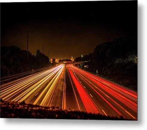 Long exposure night photograph of red and gold light trails on Interstate 64 in St. Louis, converging toward an overpass under a black sky