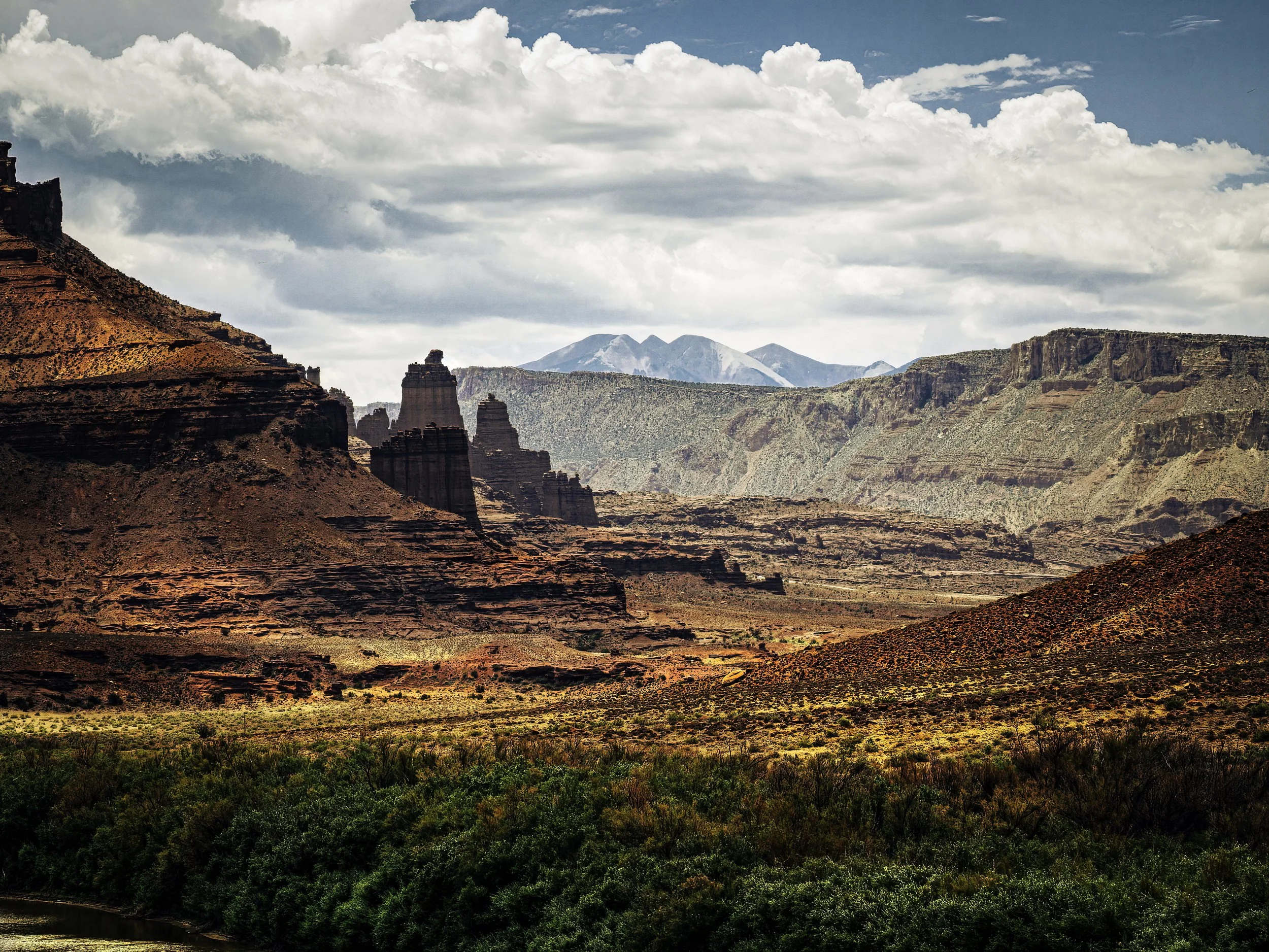 Layered red rock formations near Moab, Utah beneath towering storm clouds with distant blue mountains and desert vegetation in the foreground.