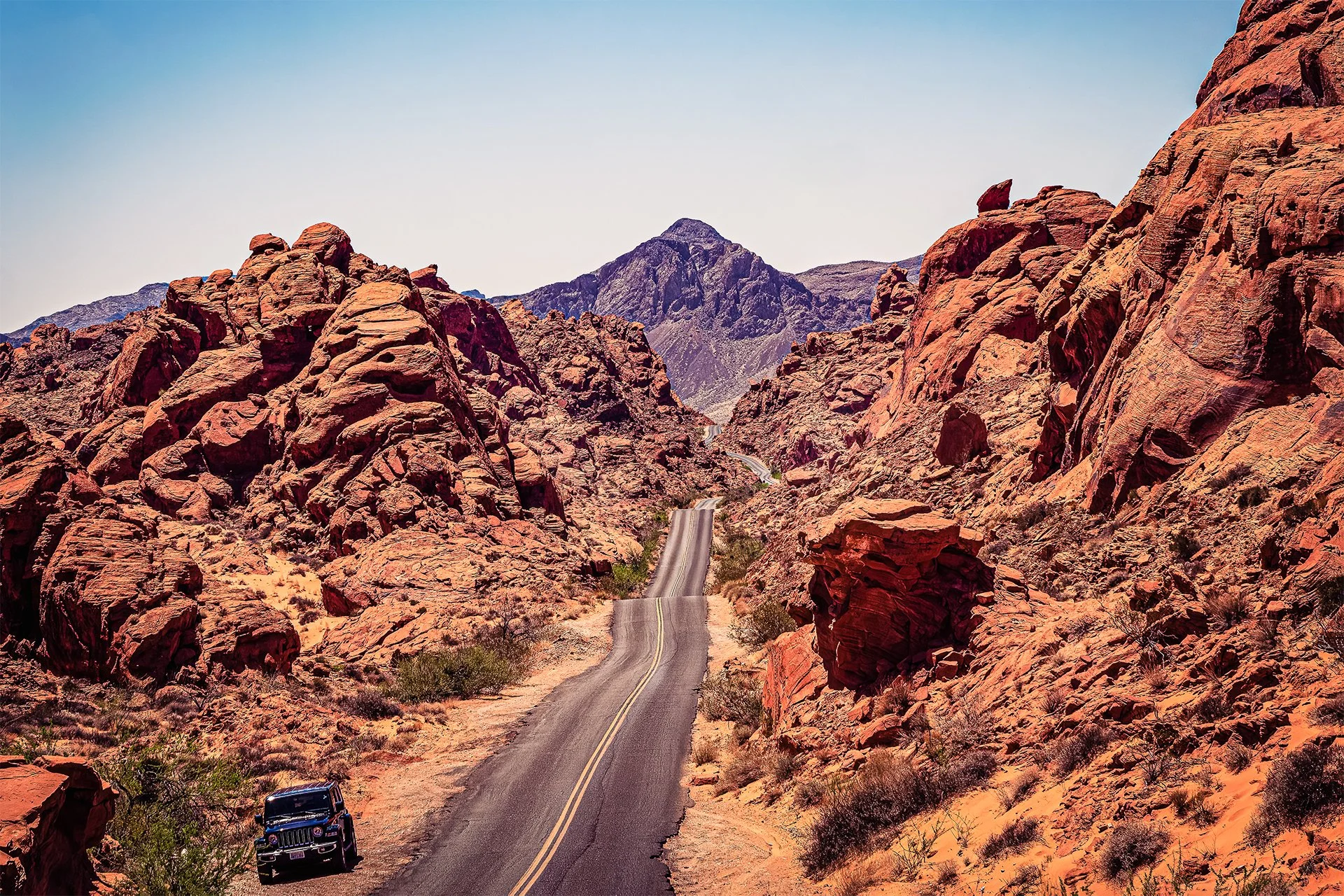 Cinematic fine art photograph of a white Jeep driving on a winding desert road through vibrant red sandstone formations in Valley of Fire State Park, Nevada.