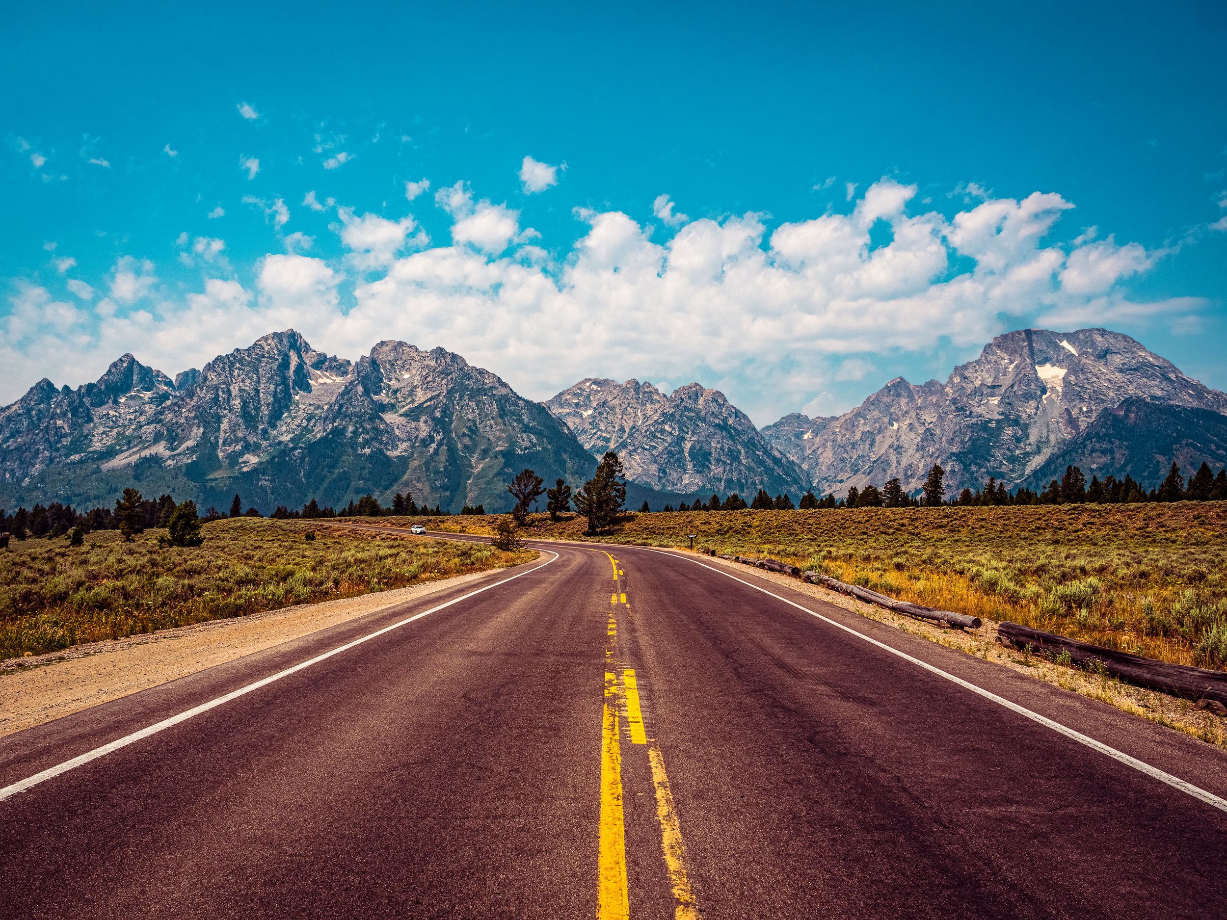 Final Teton RoFine art landscape photography print capturing an empty highway stretching toward the towering, jagged peaks of the Grand Teton mountain range under an atmospheric sky.ad - P11141 (Copy)
