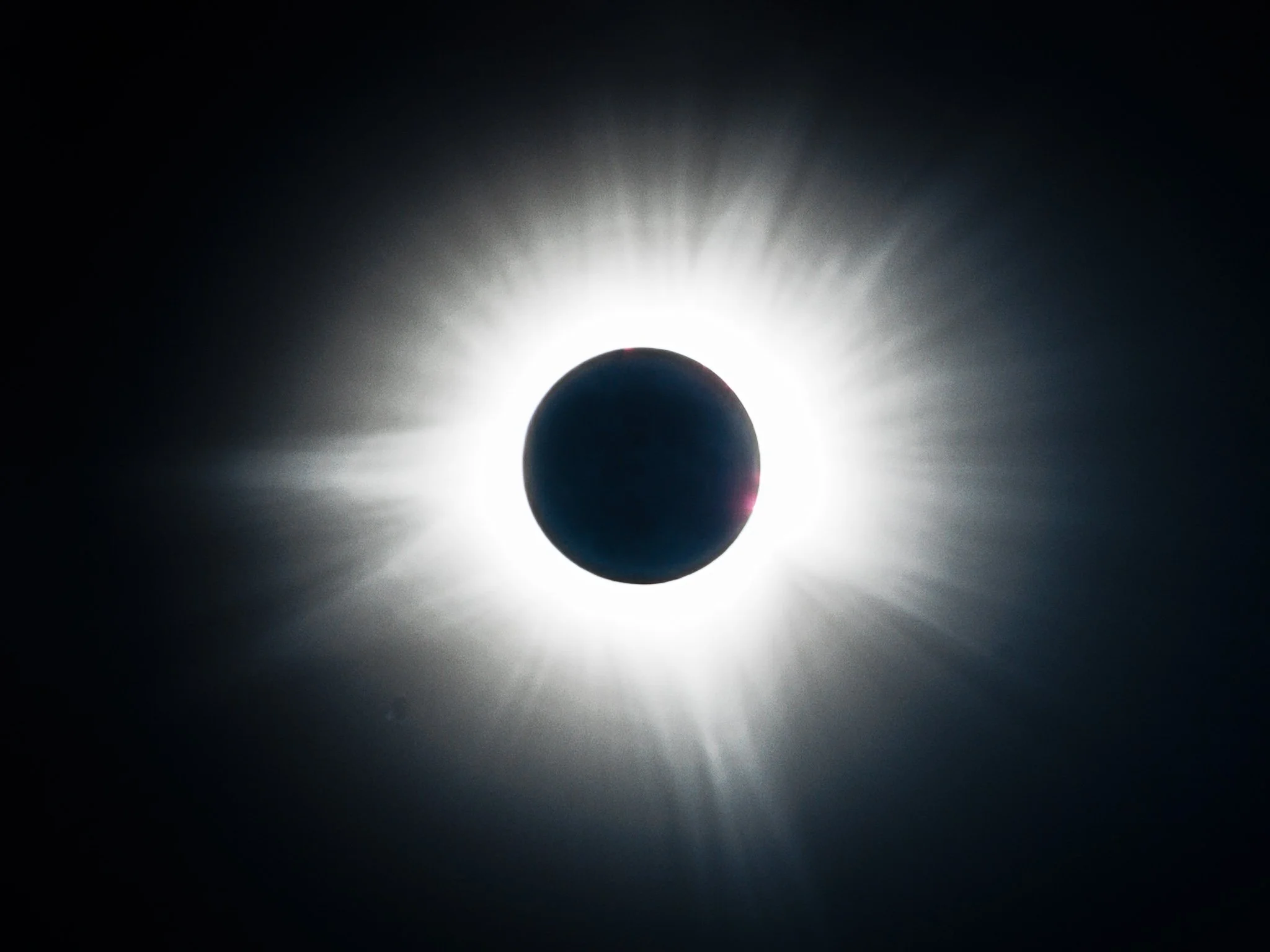 High-contrast photograph of a total solar eclipse, showing the white corona against a dark black sky.