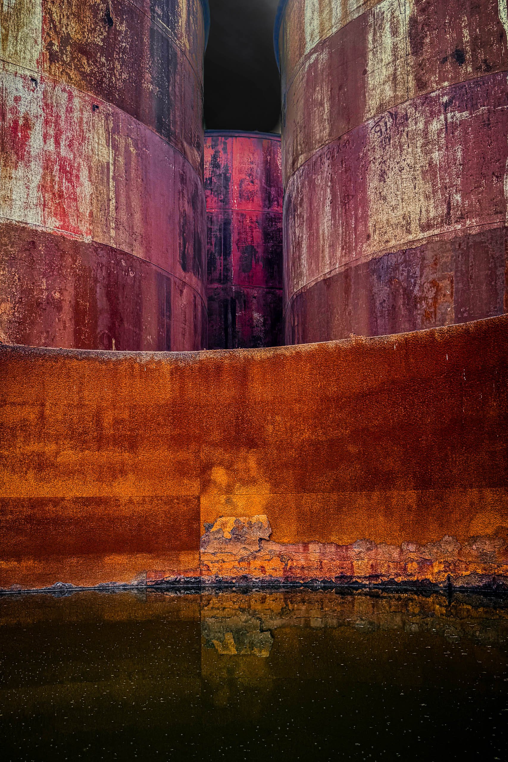 Interior view of rusted industrial storage tanks in New Haven, Missouri, curved steel walls rising above dark water toward a black sky — fine art built environment photography by Robert N Photographer.
