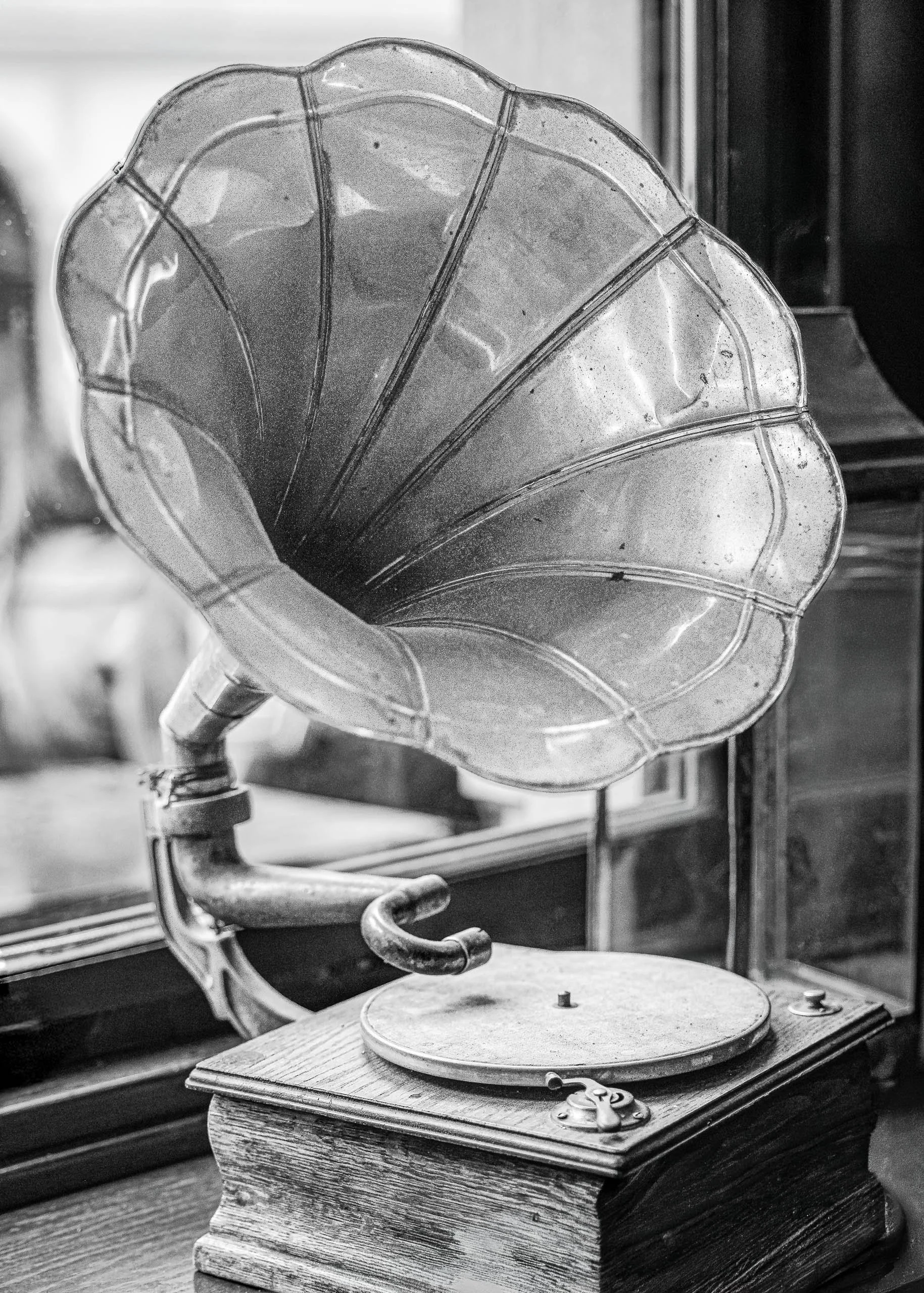 Black and white photograph of an antique gramophone illuminated by soft window light and reflective vintage surfaces.