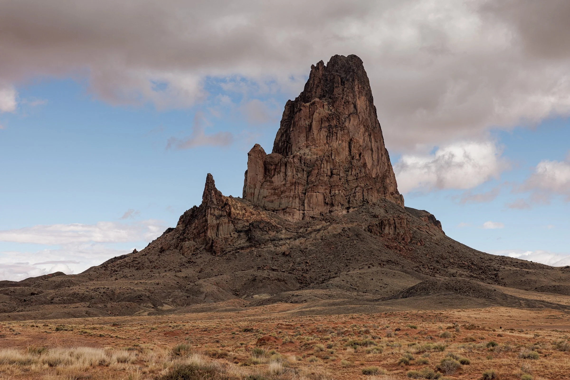 Fine art landscape photography print capturing the massive, jagged volcanic spires of Agathla Peak rising dramatically out of the high desert plains of northern New Mexico.