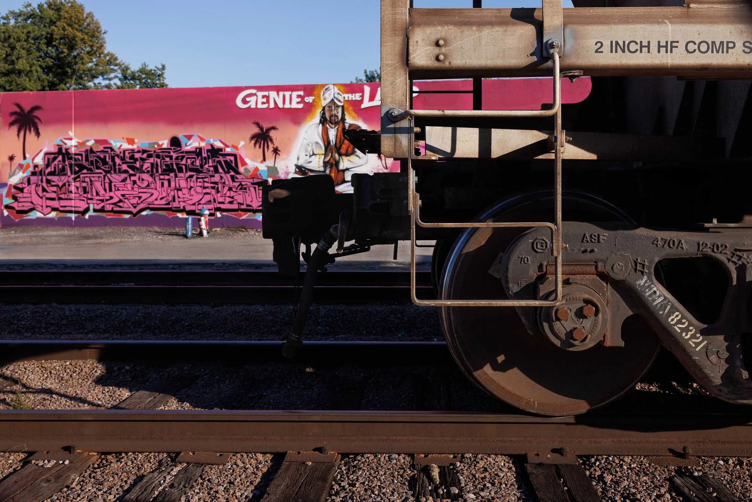 Rusted freight car beside a pink Genie of the Lamp mural with palms and rails, St. Louis, Missouri